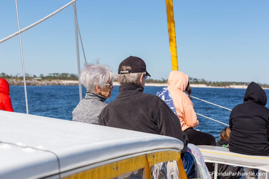 an older couple sitting on a boat wearing jackets and a hat, panama city beach, winter