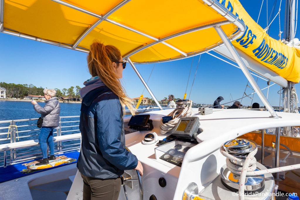 a women with ginger hair and a navy blue wind breaker jacket driving a boat