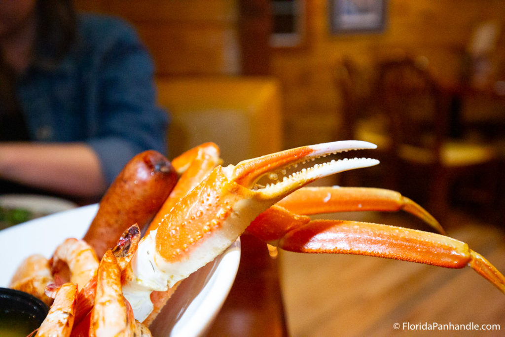 two crab hands poking out of white plate next to some sausage and shrimp