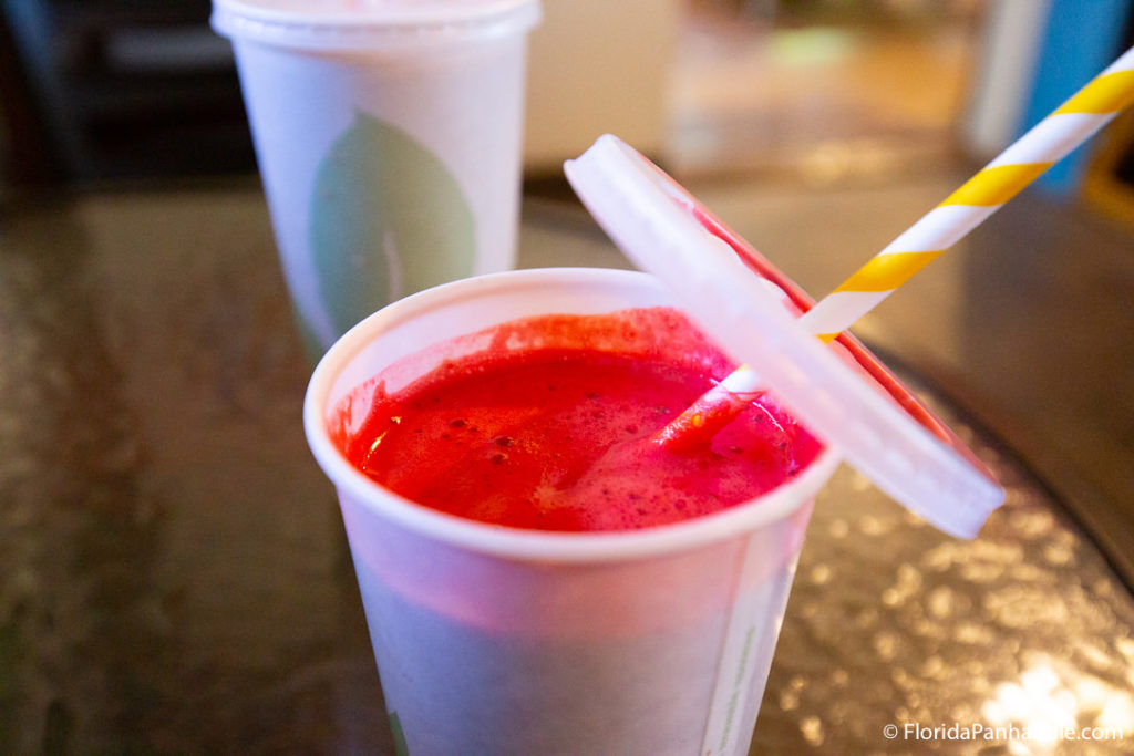 a cup of bright red juice with the lid slightly off and a yellow spiral straw at Lotus Health Food Cafe & Juice Bar