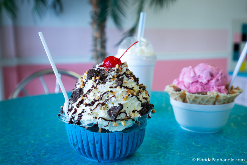 a clear plastic bowl full of ice cream with whipped cream, oreo chunks, and a cherry on top