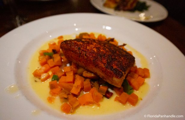 fish on top of chopped carrots and creamy sauce inside of white plate