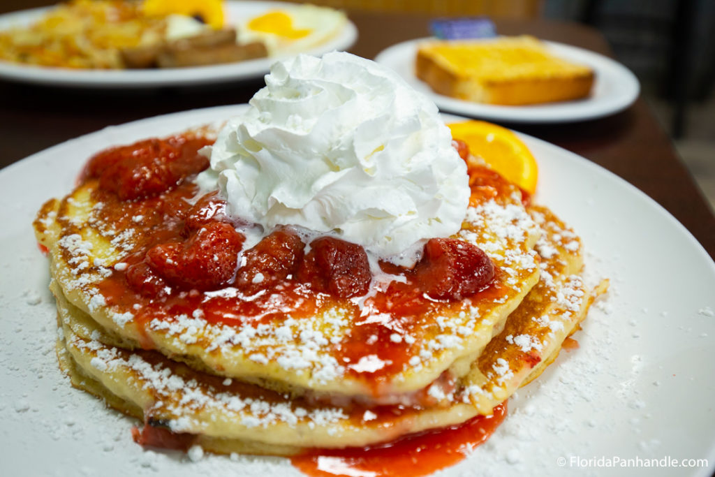 a plate of pancakes with strawberry syrup and whipped cream on top at Pancakery of PBC