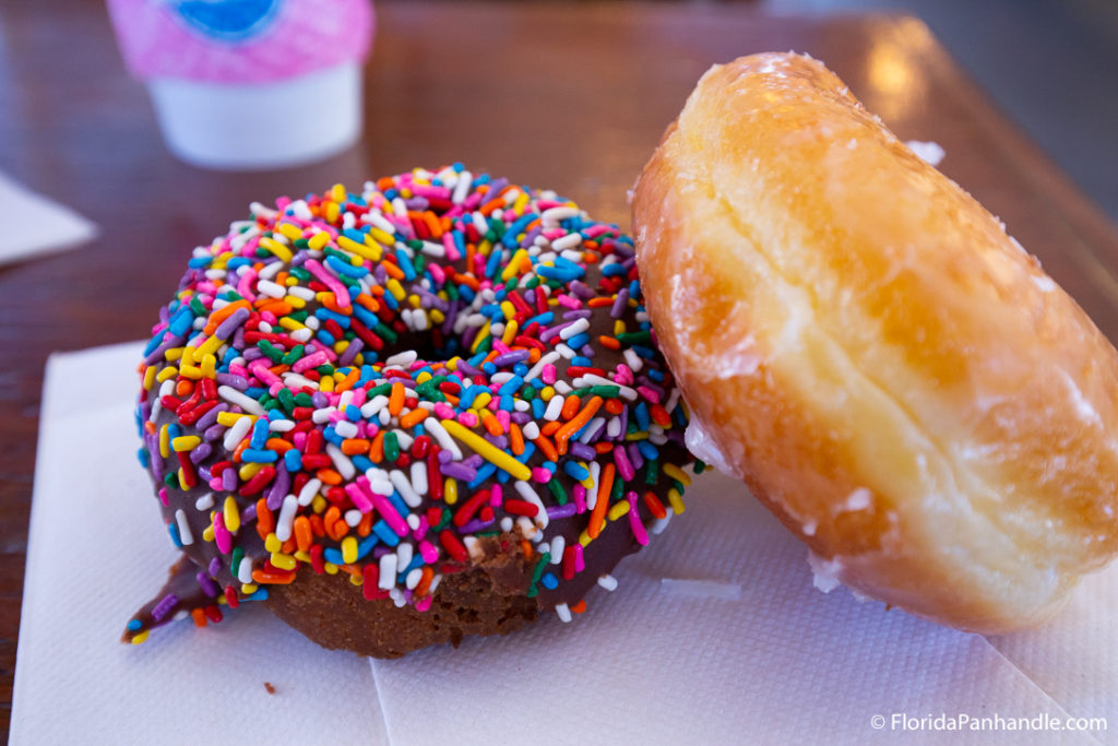 a chocolate donut with chocolate frosting and rainbow sprinkles on top, next to a glazed donut at Thomas Donut and Snack Shop