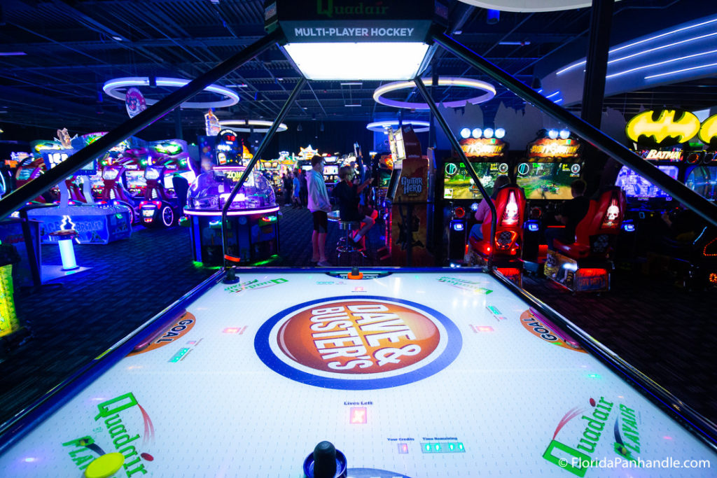 an air hockey table with a giant Dave & Busters logo in the middle of it at an arcade venue with only black lights on