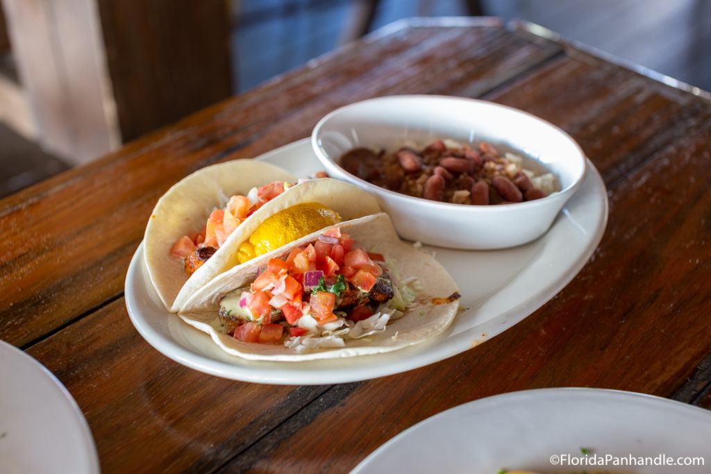 two tacos side by side with some tasty seafood and a lemon in between next to a side dish