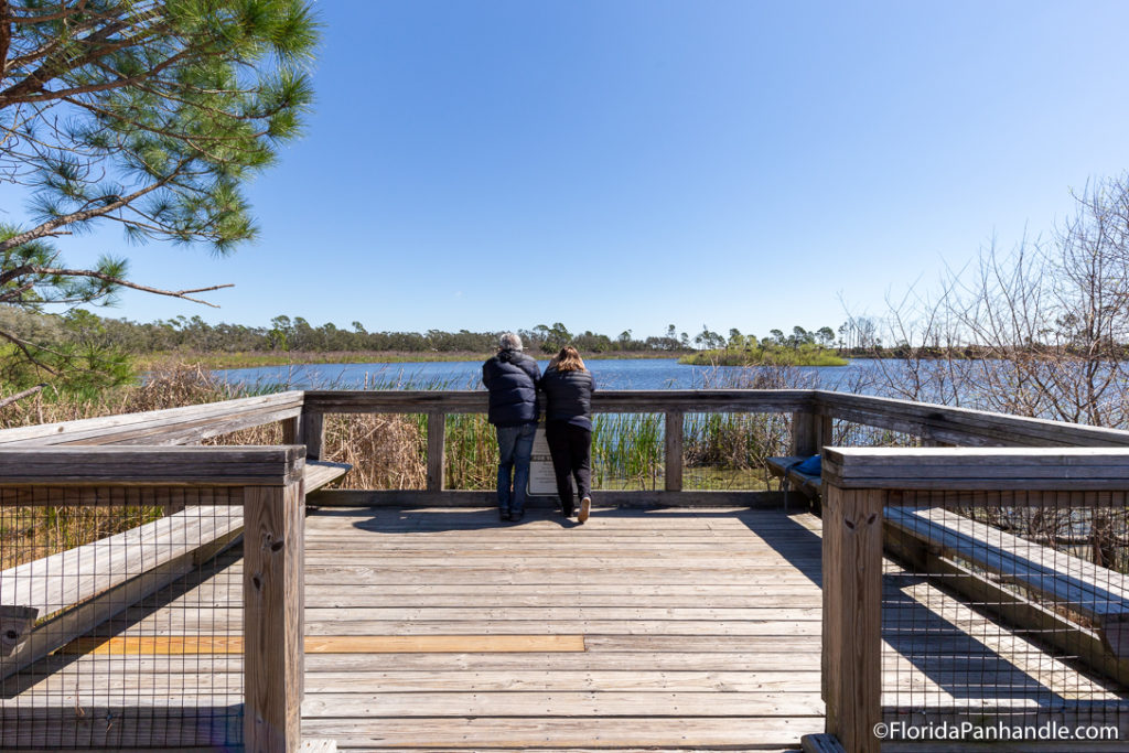 a couple standing at the end of a lookout on the bridge looking out to the water