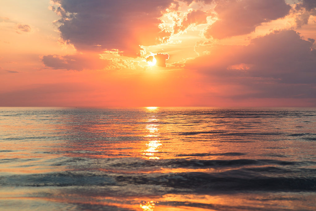 view of the ocean during the sunset, with pink, purple and orange hues