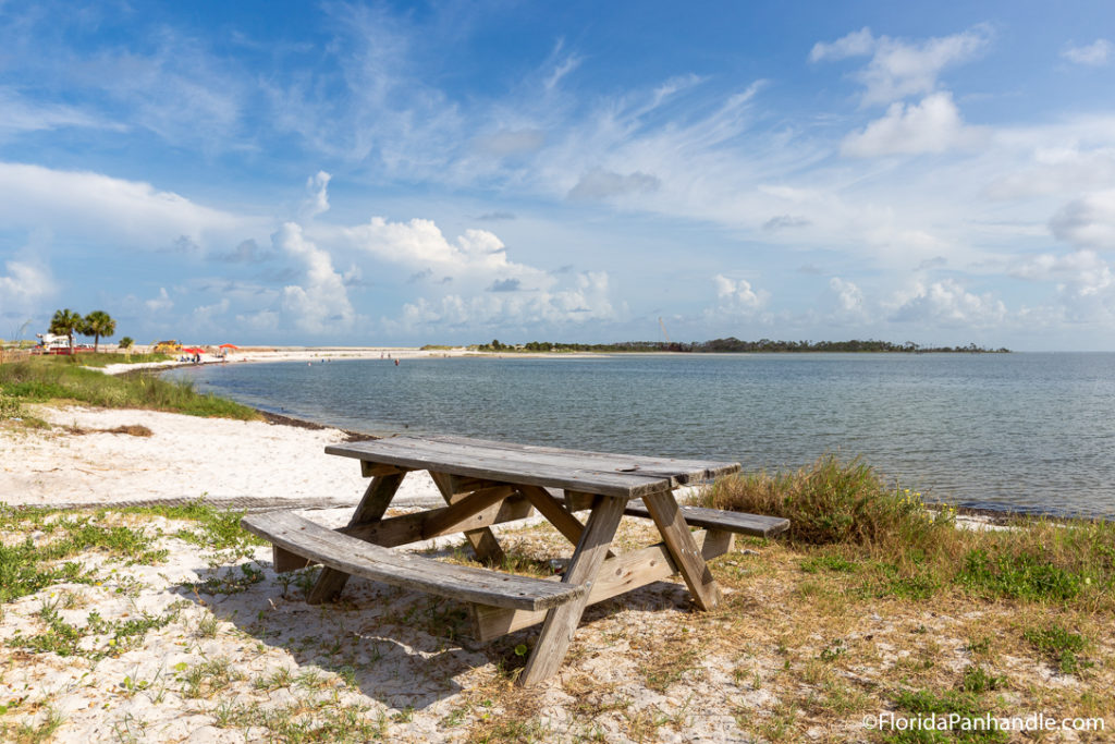 a picnic bench off the beach in the sand on a sunny day