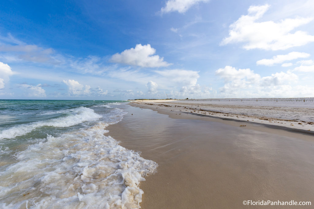 waves washing up on the shoreline of a brown sand beach on a sunny day with blue skies