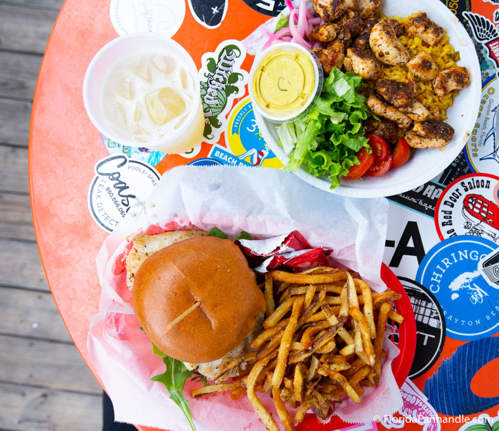 a burger with a side of fries and a plate of grilled chicken on a bed of yellow rice with a side salad 