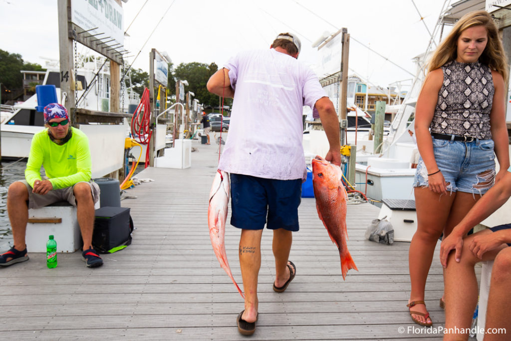a man holding fish walking down a boardwalk, deep sea fishing in destin, florida