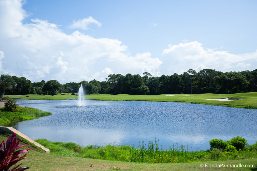 a big pond with a water fountain in the middle and surrounded by large open areas of green grass and sand bunkers during the day