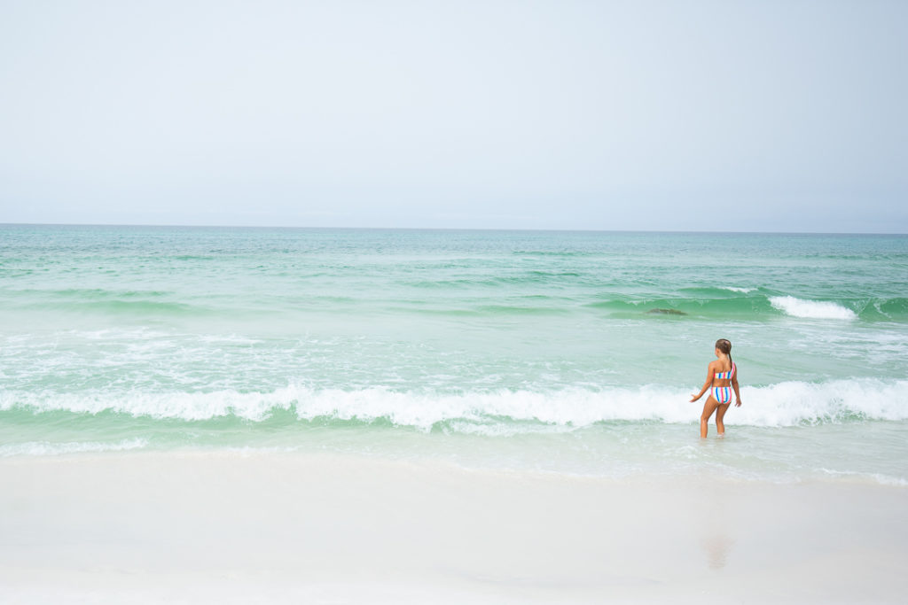 young girl wearing colorful striped bathing suite playing in the water on the beach