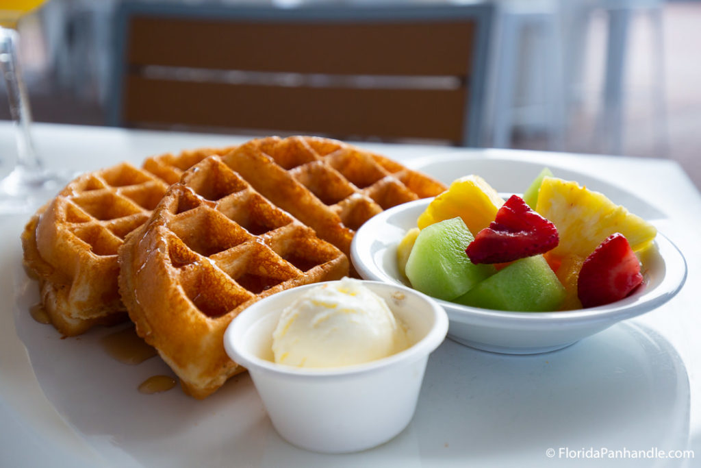 two halves of a waffle on top of white plate next to fruit and butter