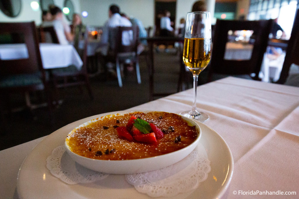 a creme brulee with sliced strawberries on top with a glass of champaign on the side