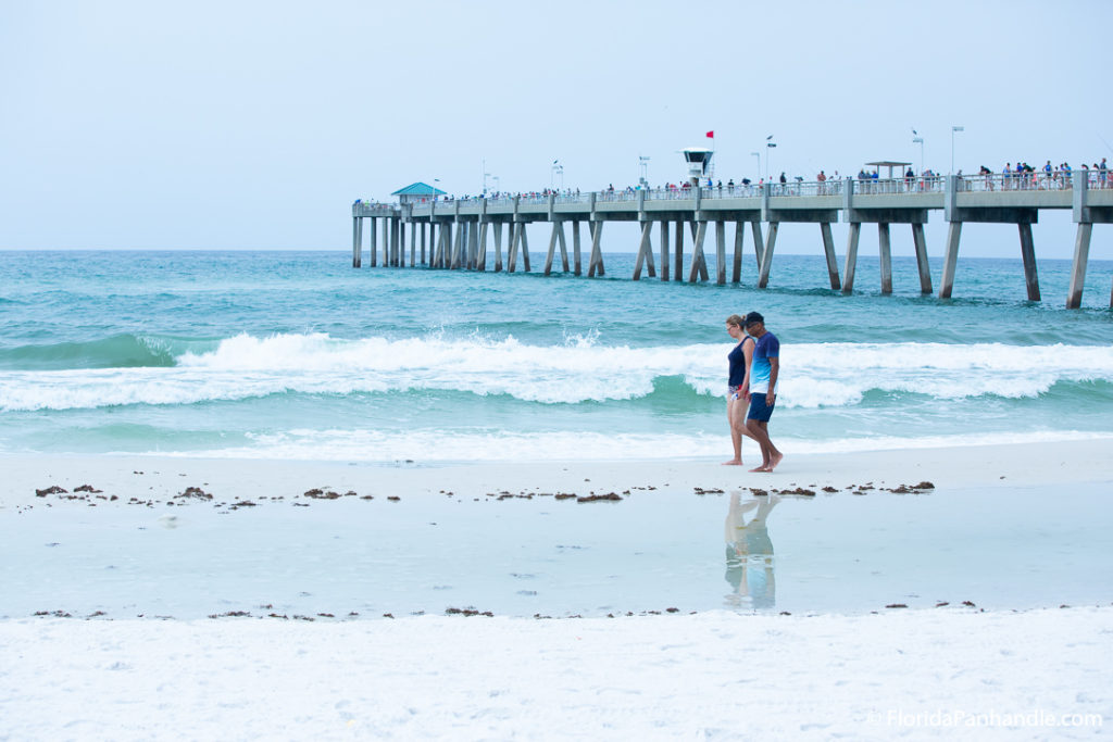 two people walking along the shoreline with a pier full of people behind them at Okaloosa Island in Florida