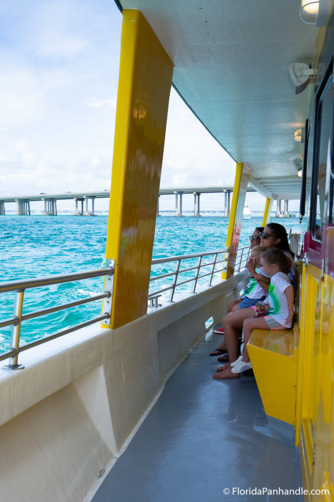 two kids a woman sitting on a bench on the side of the boat looking out unto the ocean