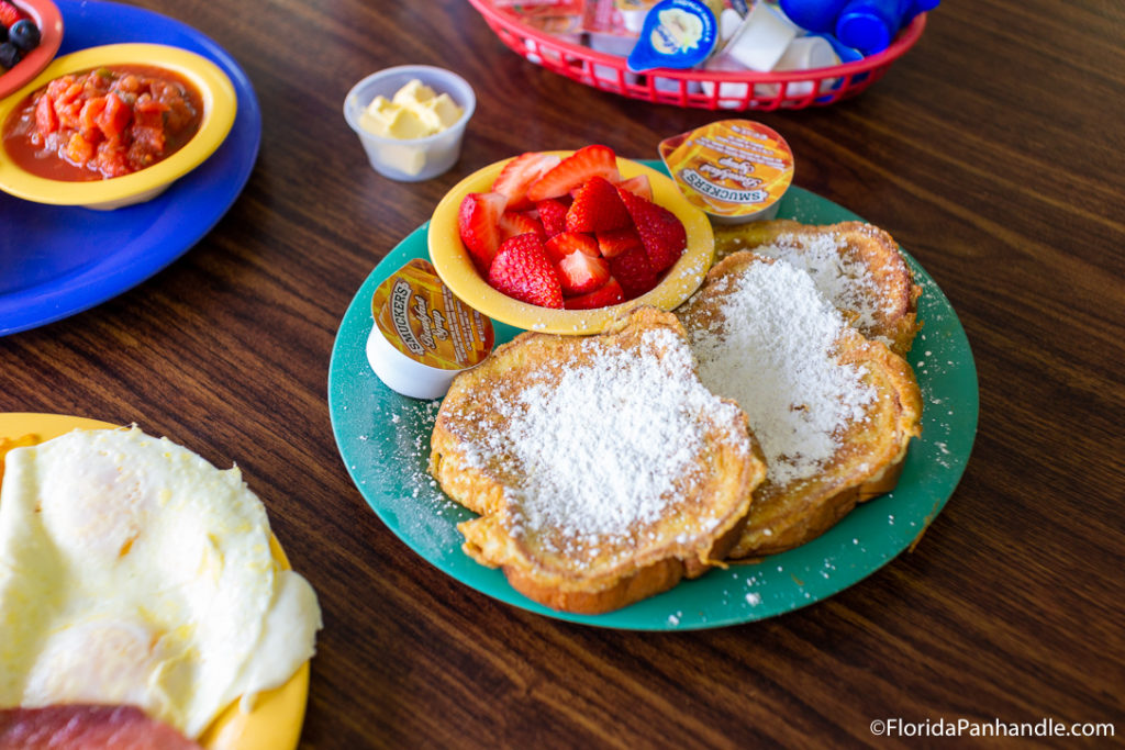 a plate of french toast with powdered sugar in top and a bowl of fresh sliced strawberries on the side at Jesse's Place