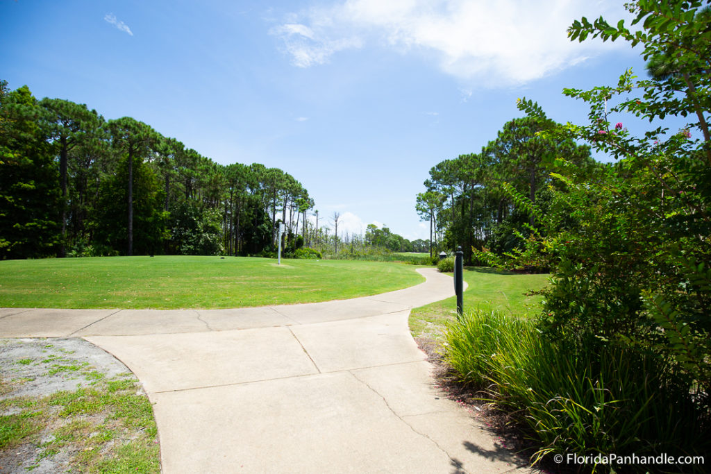 sidewalk leading to a open green area of a golf course