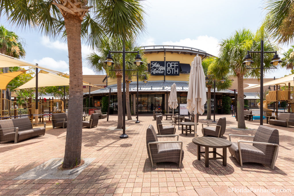 lounge chairs and tables with closed umbrellas in front of yellow shopping store at Silver Sands Premium Outlets 