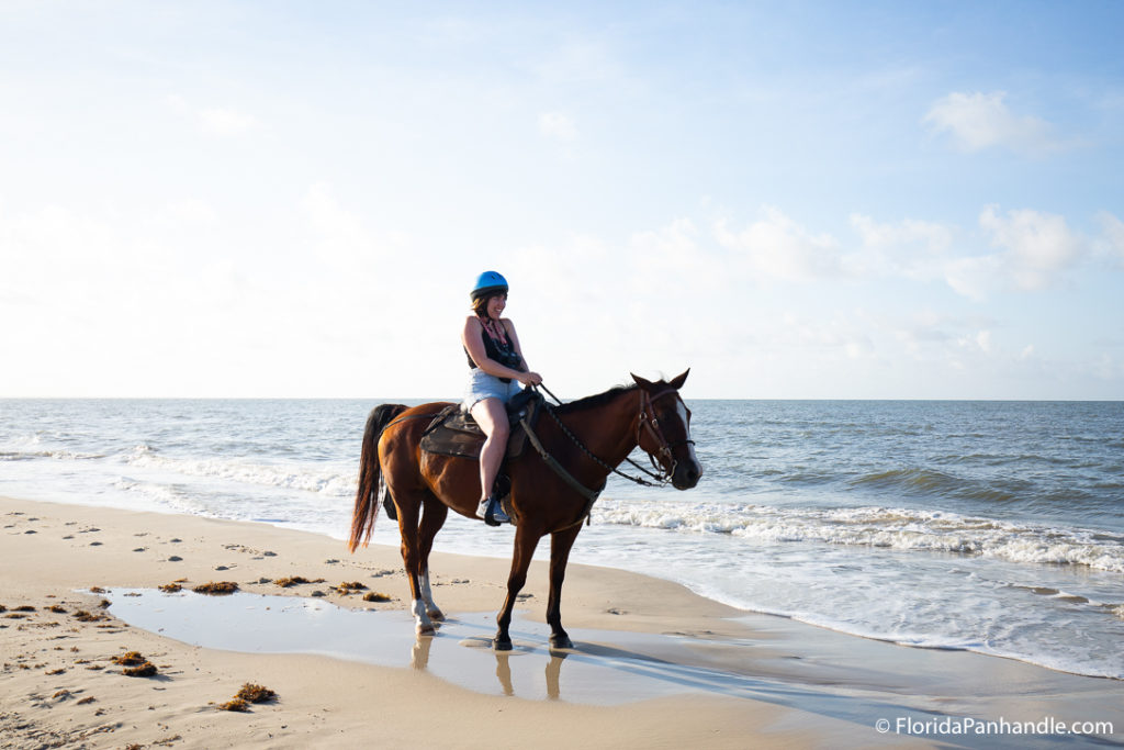 woman riding on horseback on the beach with waves brushing the shore