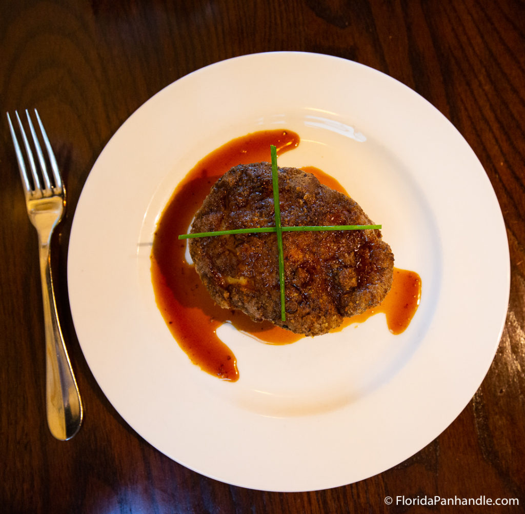 a steak with two chives on top in an X shape with the steak juices leaked all over the white plate