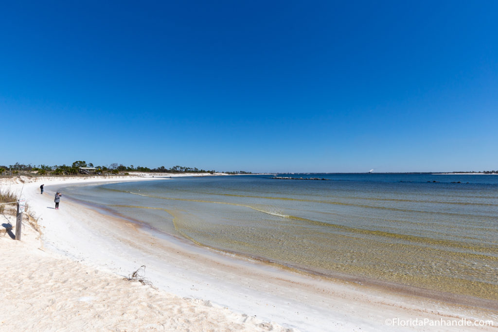 two people on the beach photographing the scenery during the day with extremely clear bright blue skies