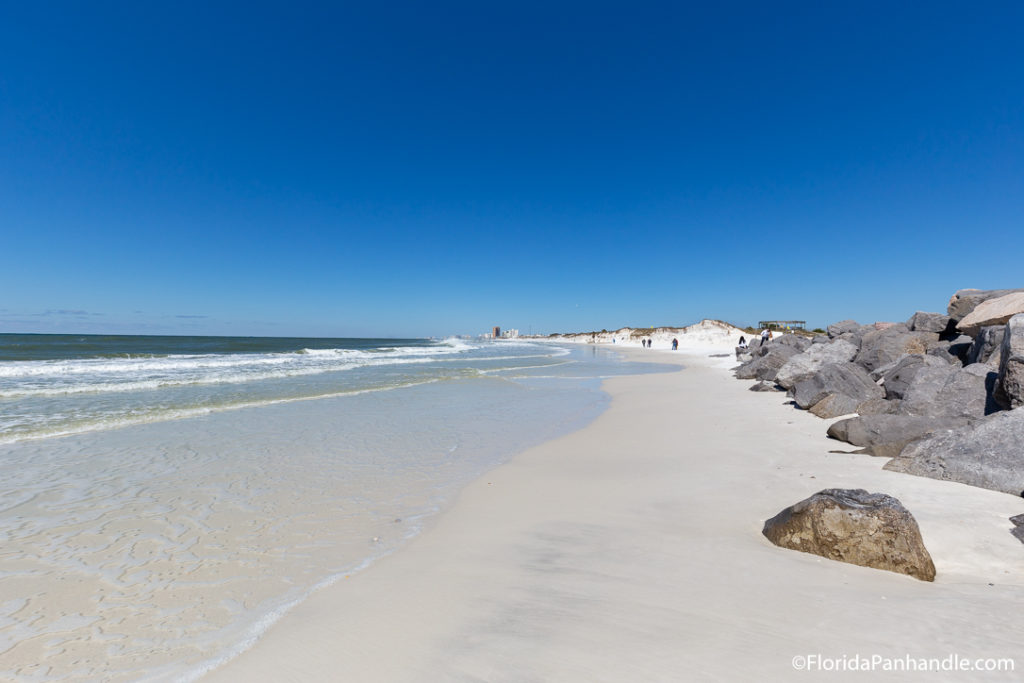 an empty beach with rocks along side the shore on a sunny day with bright blue clear skies