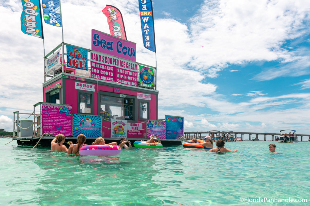bright pink water bar with people in floaties surrounding it with bridge in the background