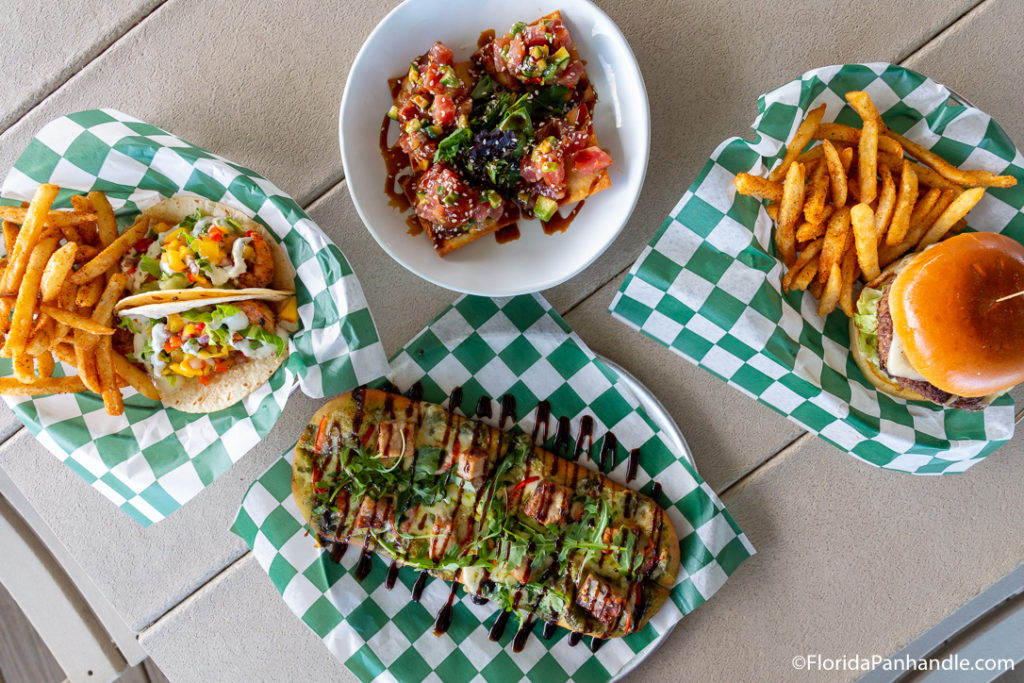 many different plates including a balsamic flatbread, a burger with a side of fries sushi bites and soft shell tacos with a side of fries at Laguna's Beach Bar & Grill