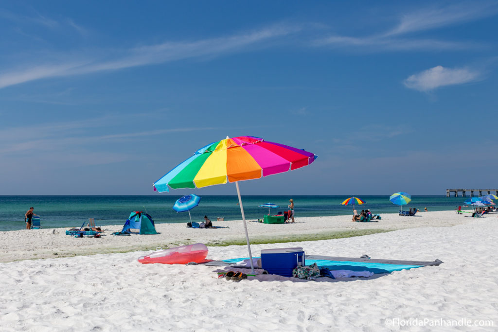 a rainbow umbrella in the sand with a towel and cooler underneath