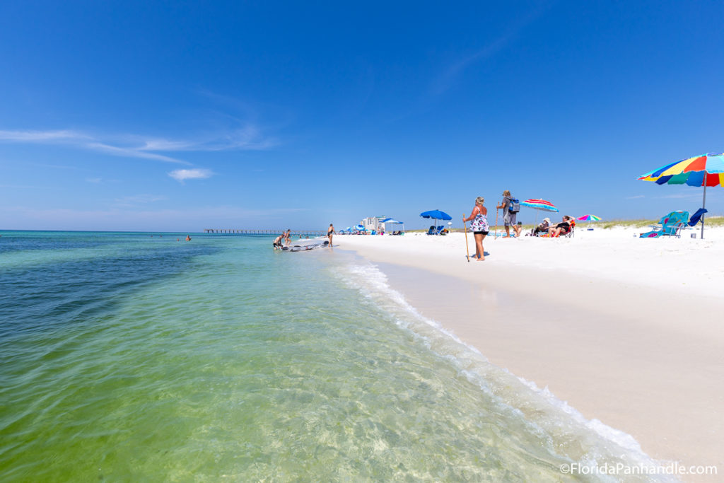 a busy beach with turquoise clear waters and white sand at Navarre Beach Florida