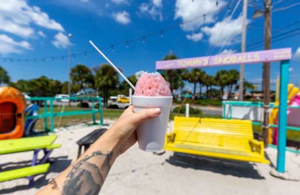 someone holding pink shaved ice in a white styrofoam cup with a straw in it