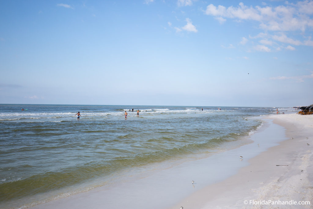 waves pulling back from shore line while people walk in the water in Blue Mountain Beach FL