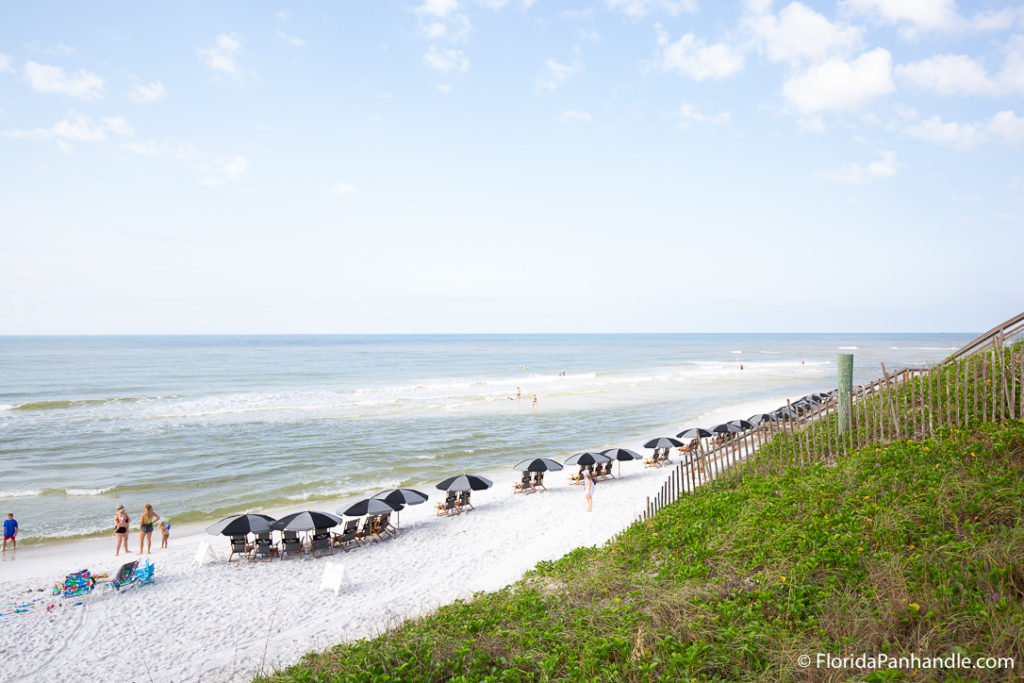 black and grey beach umbrellas on top of white powdered sand with waves crashing to shore in the background and people standing