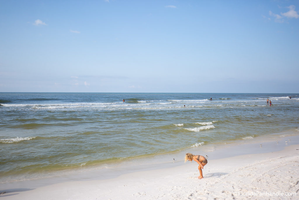 little girl closely looking at the sand at a beach in florida with waves crashing in the background