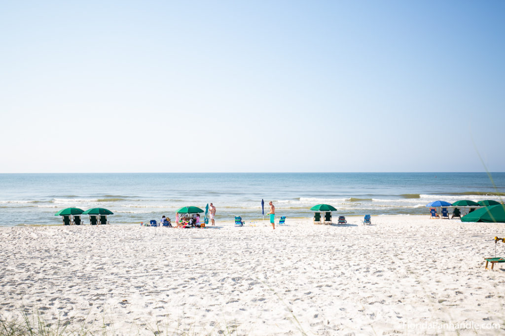 a family at the beach sitting together under an umbrella at Inlet Beach in Florida