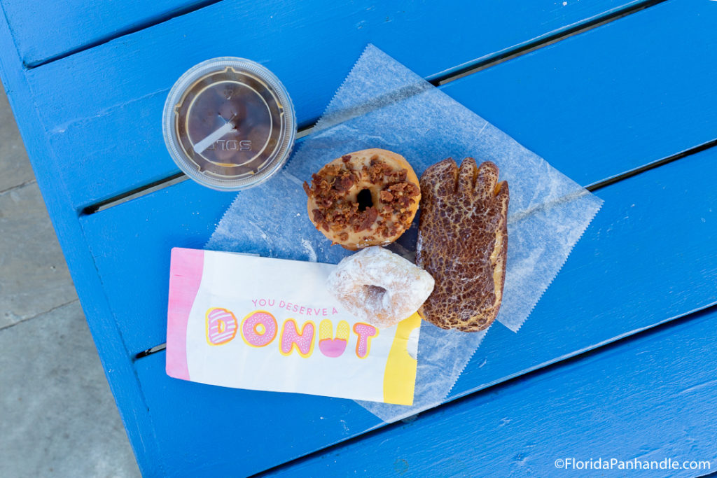 three donuts and a cup of iced coffee on a bright blue bench table at Charlies Donuts in 30A