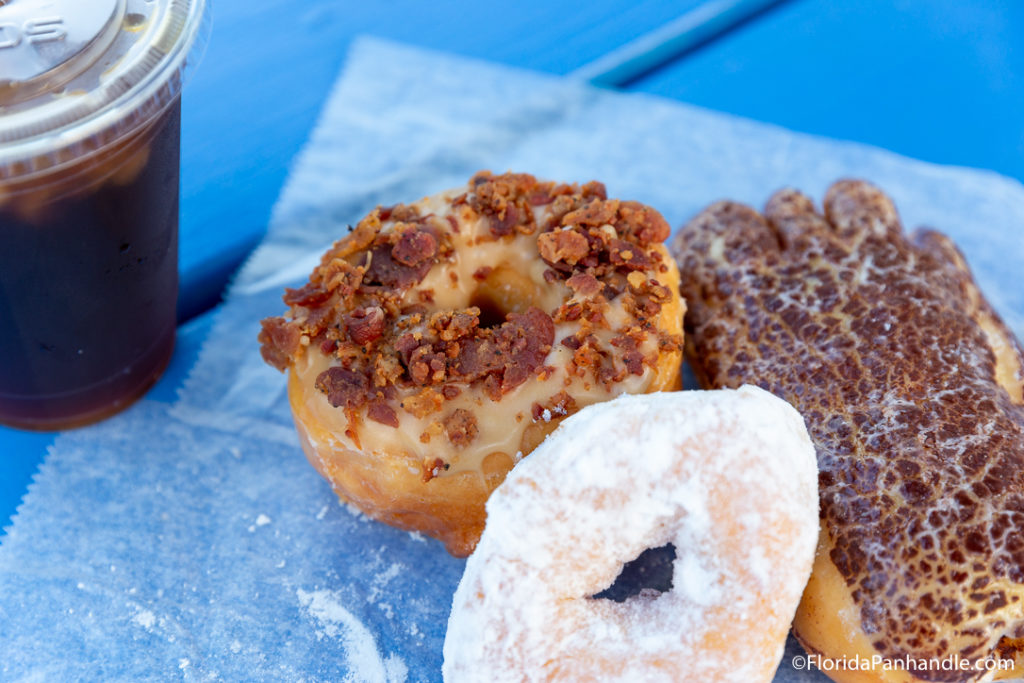 a maple frosted donut with bacon bites on top, a powdered donut and a chocolate frosted bear claw donut at Charlie's Donut & Yogurt Truck