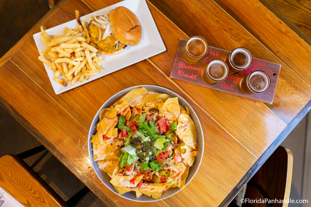 a platter of nachos, burger with a side of fries and a flight of beer