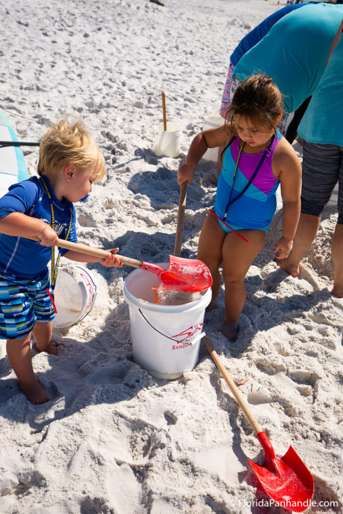 little boy and girl shoveling sand into a bucket at the beach