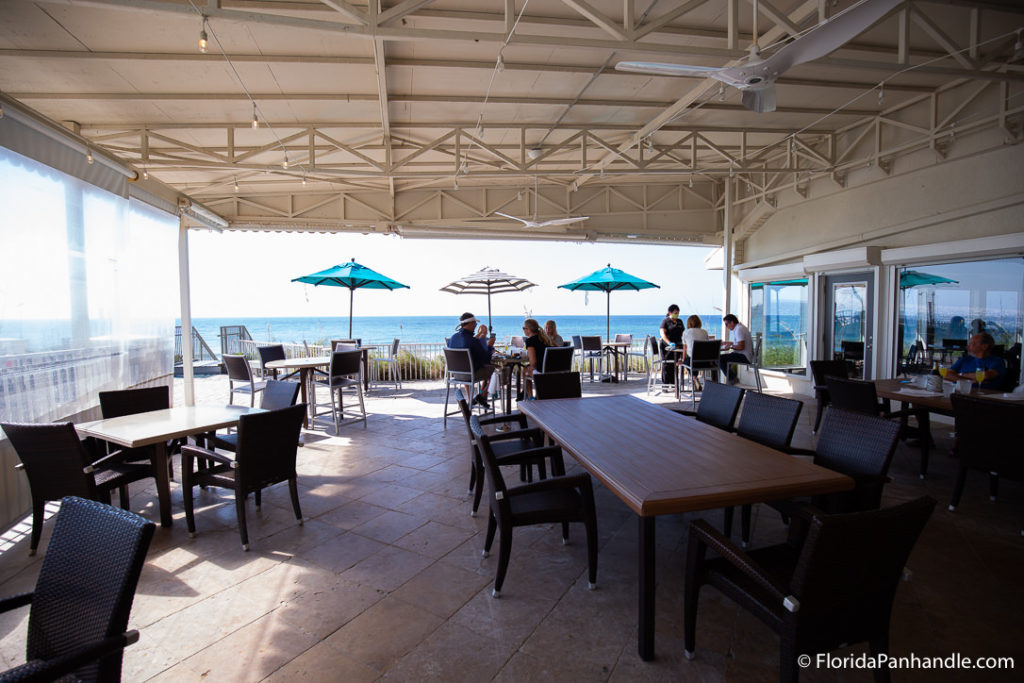 an outdoor restaurant with ocean view and table with blue umbrellas and striped umbrellas