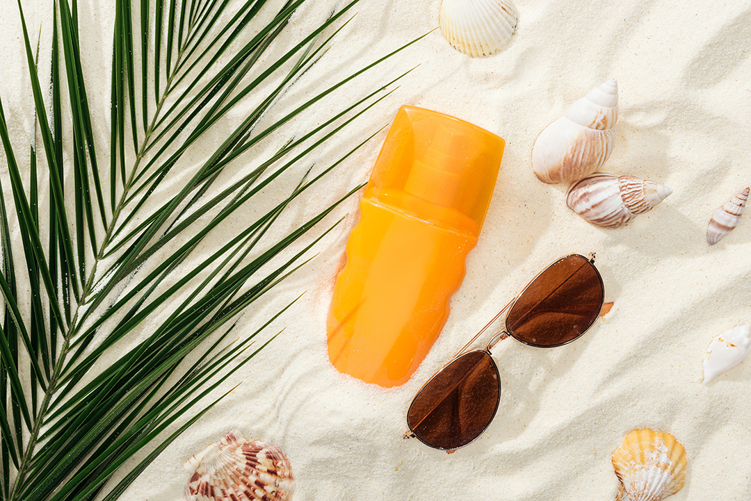 glasses an orange bottle of sunscreen and seashells in the sand