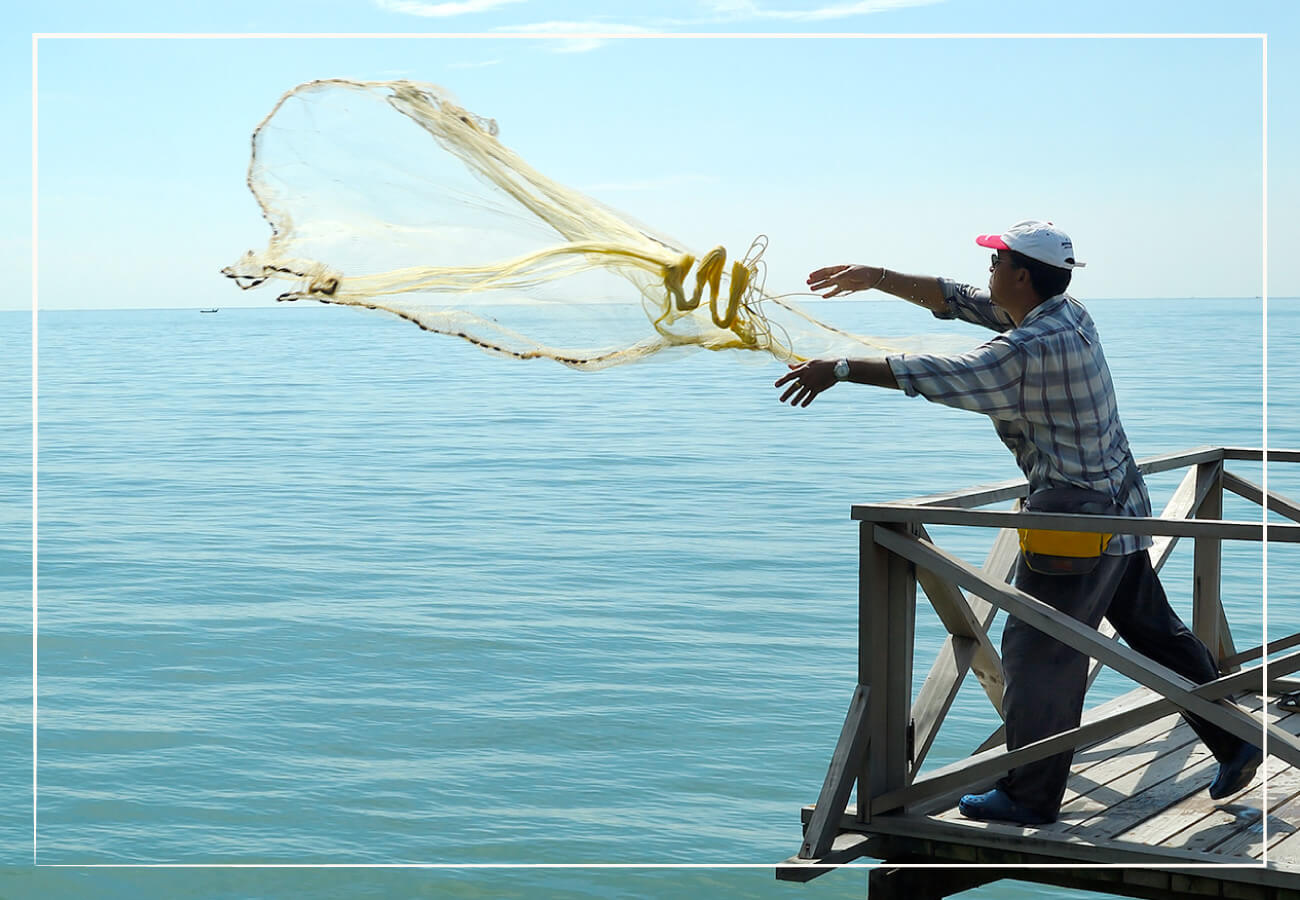 man throwing fishing net into the ocean from a pier on a sunny day with blue skies