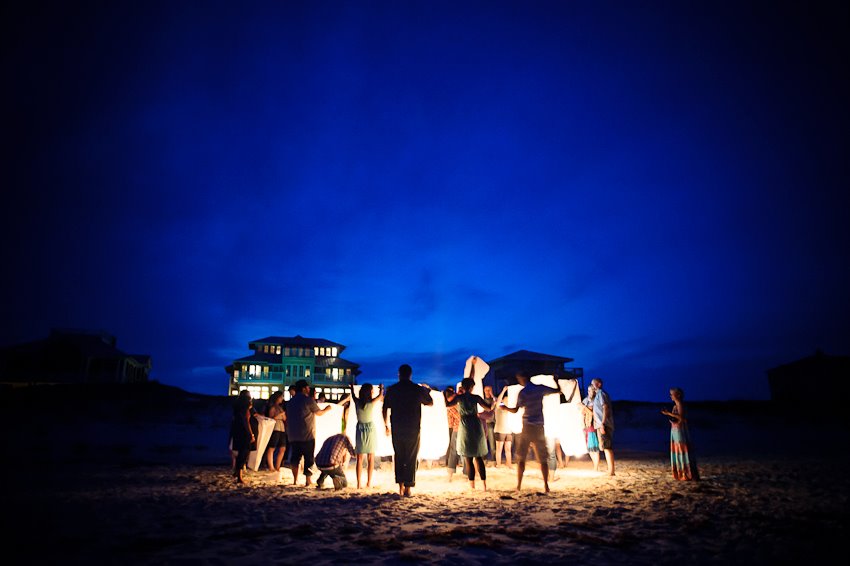 group of people on a private beach at night with lighted floating lanterns