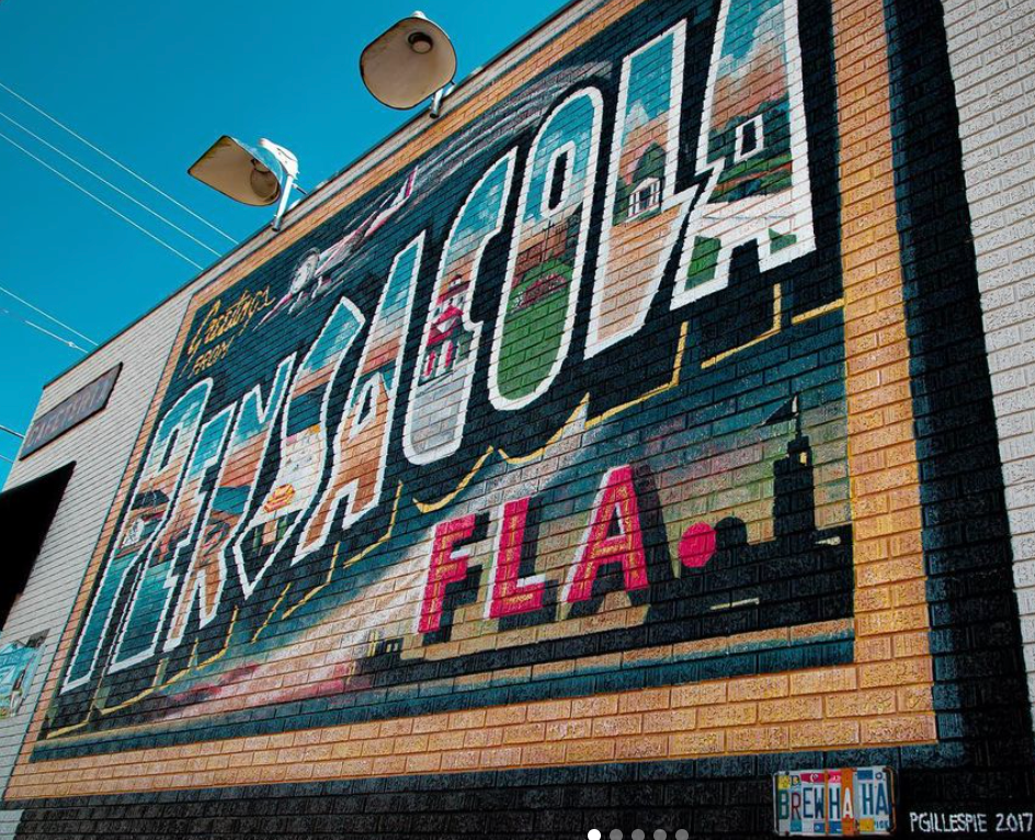 a giant mural on a brick wall that looks like a post card and says Pensacola FLA.