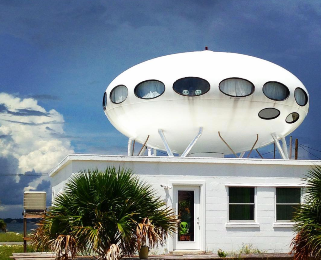 a white house that has a white UFO connected to it with two little aliens peeping out the window