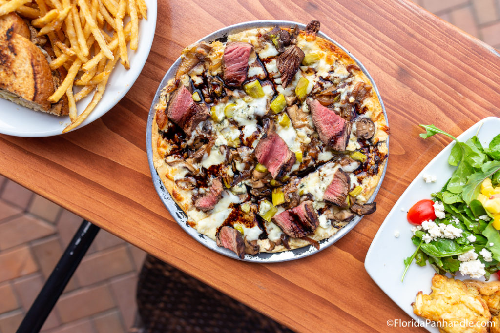 pickle pizza with steak and steak sauce next to two other plates