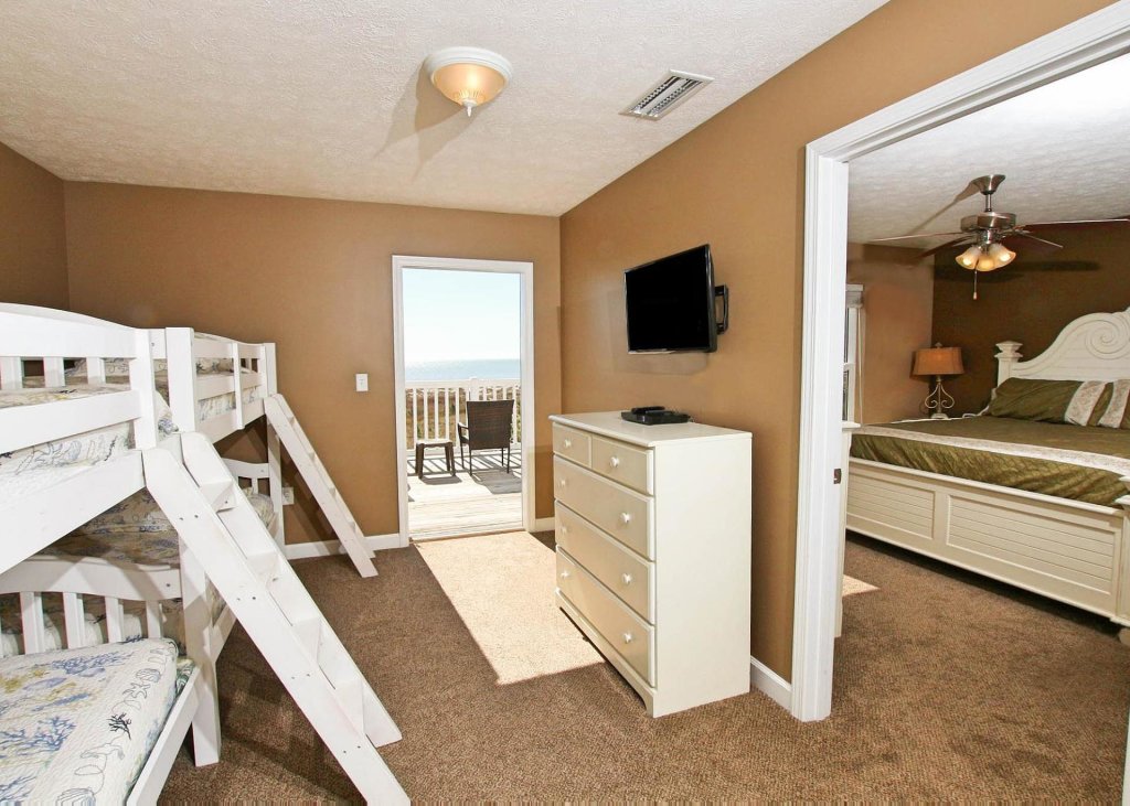 bunk beds to the left and master bedroom to the right with dresser in between and tv, door leading to the beach in florida